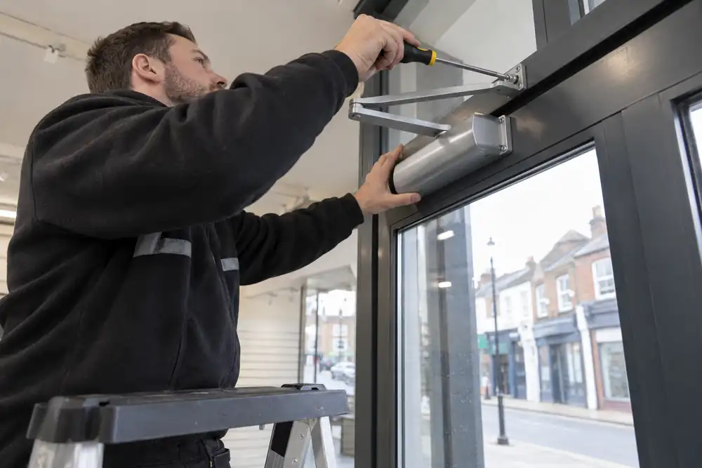 Technician fitting a closer to a commercial glass shop door